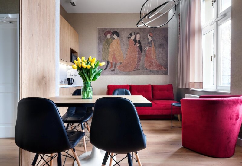 Modern hotel lounge with red sofa and armchair, wooden table with black chairs and yellow tulips.
