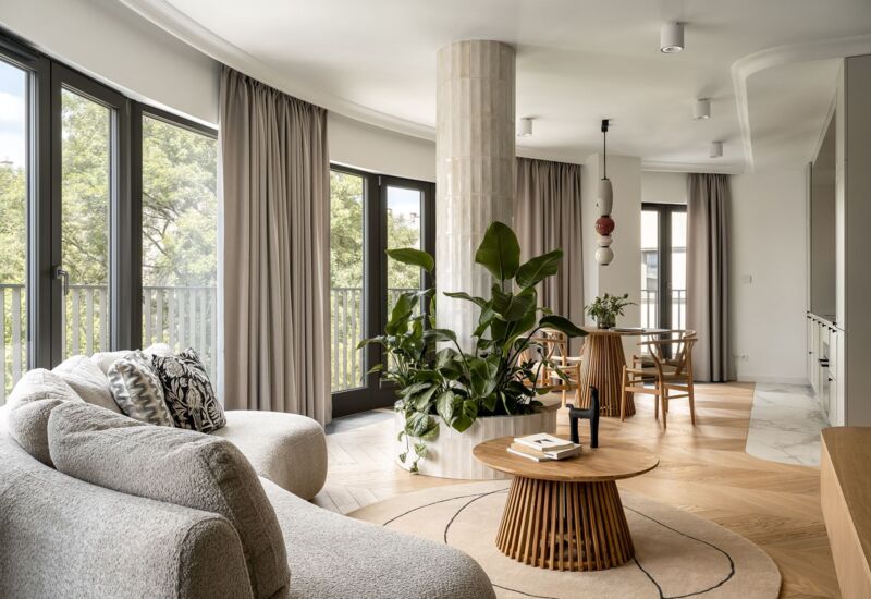 Modern, bright hotel lounge with large windows, comfortable sofa, table with decorations and green plants.