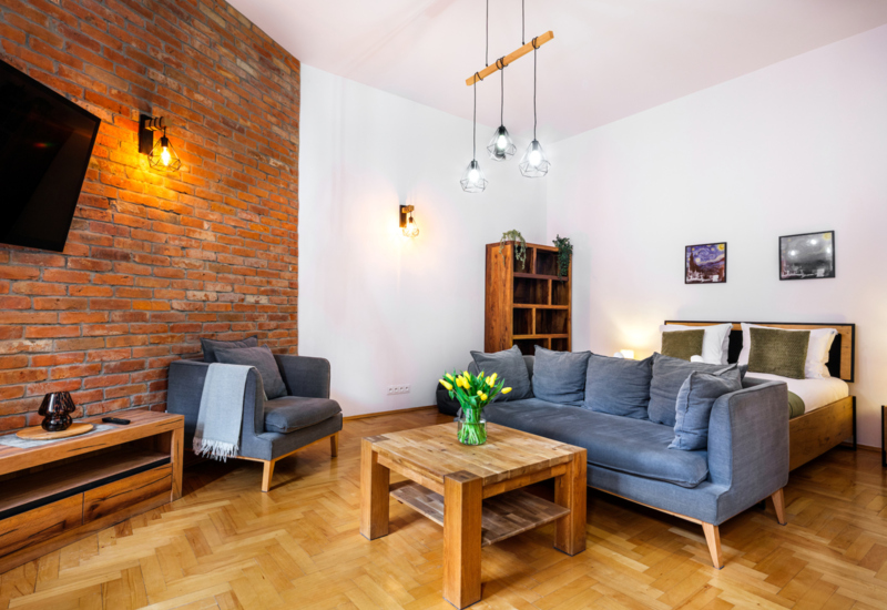 Cozy hotel room with double bed, modern gray sofa, wooden side table and decorative brick wall.