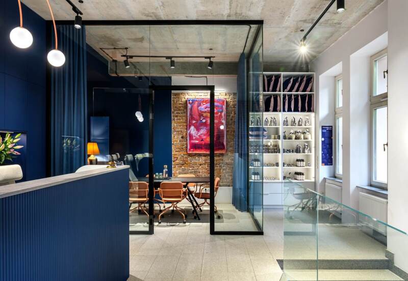 Modern hotel reception with navy walls, glass conference room and shelves with hotel products.