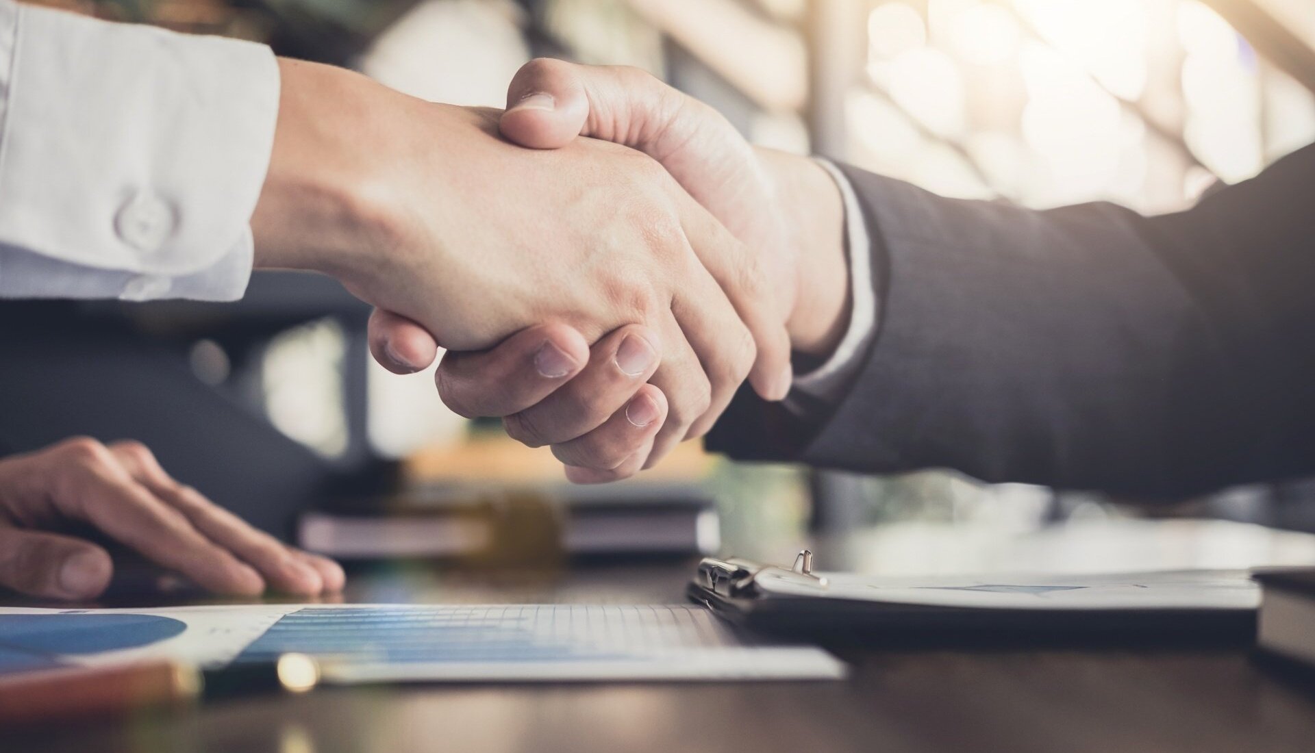 Dłonie dwóch osób w uścisku podczas biznesowego spotkania w jasnym, nowoczesnym biurze hotelowym