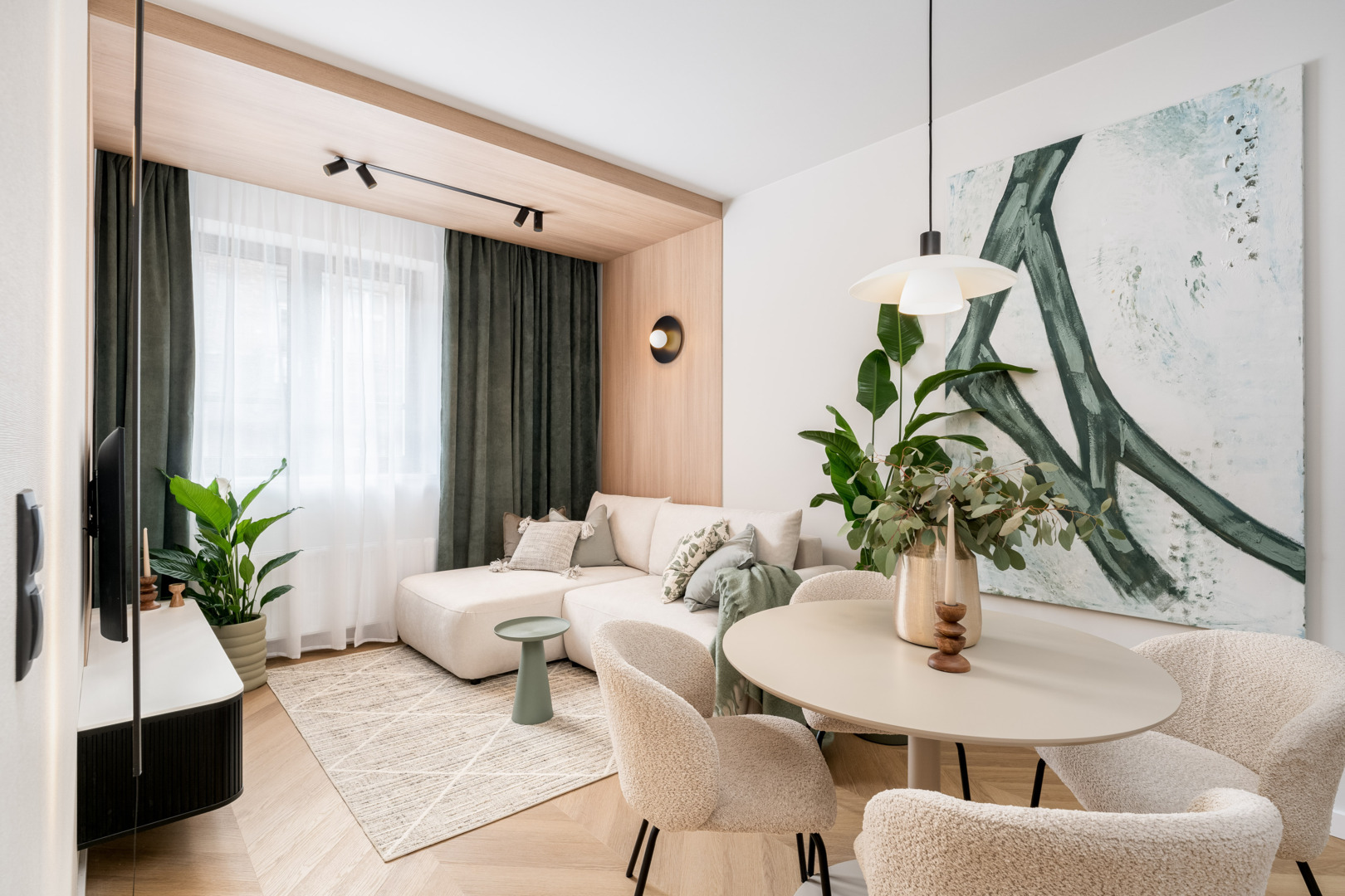 Nowoczesny pokój hotelowy z jasną sofą, stolikiem, okrągłym stołem z kwiatami i dużym abstrakcyjnym obrazem na ścianie