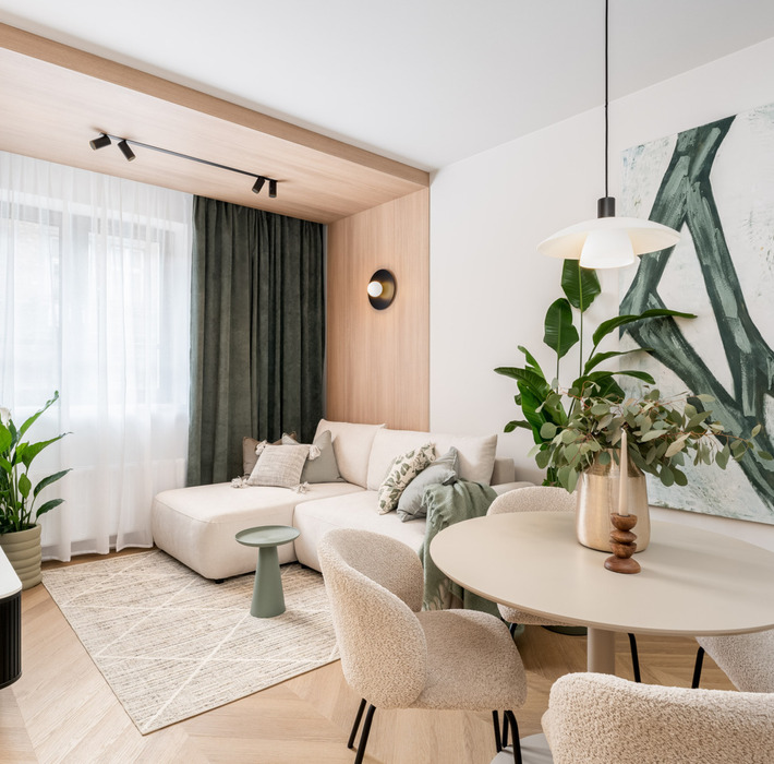 Nowoczesny pokój hotelowy z jasną sofą, stolikiem, okrągłym stołem z kwiatami i dużym abstrakcyjnym obrazem na ścianie