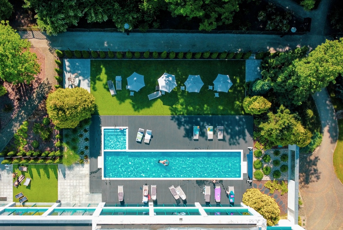 Rectangular hotel outdoor pool on a sun terrace with loungers, parasols on a grassy lawn and a guest floating on a ring.