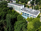 Hotel with three-story guest wing and glass-front spa, outdoor pool with loungers and balconies overlooking dense parkland