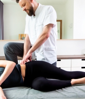 Therapist giving side-lying therapeutic massage to woman in a modern spa treatment room, spinal model and calm cabinetry in background.