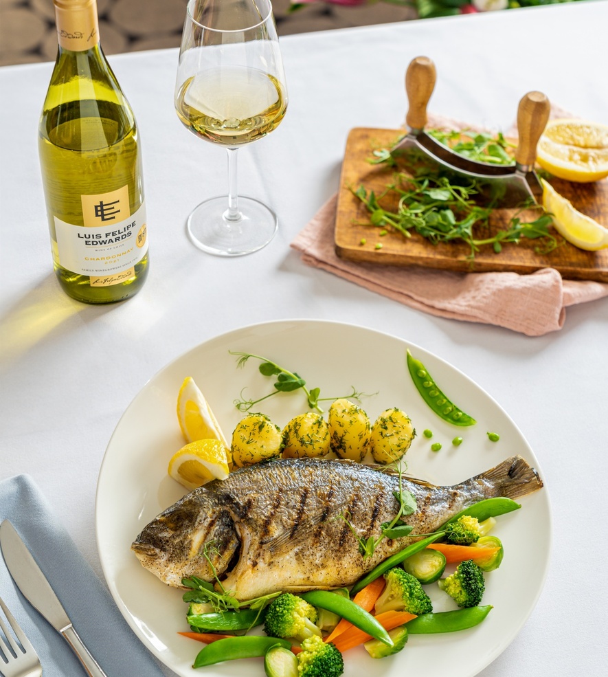 Grilled whole sea bream with dill potatoes and seasonal vegetables, paired with a glass and bottle of Chardonnay.