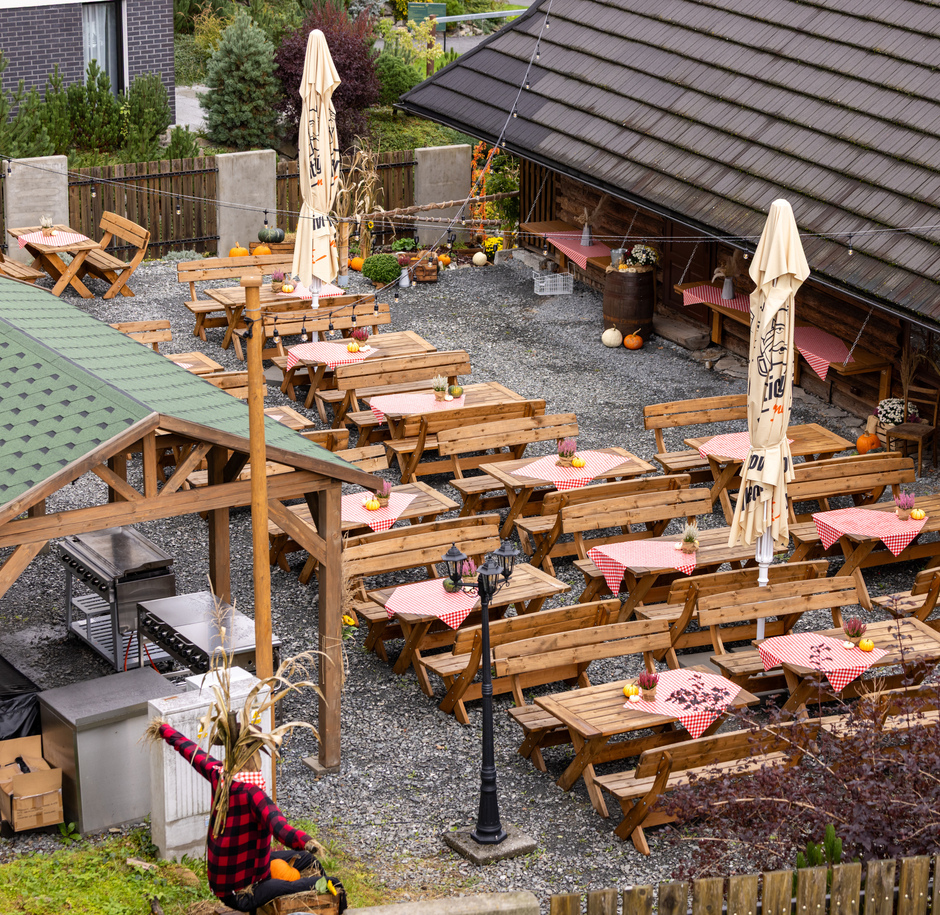 Rustykalny ogródek restauracyjny z drewnianymi ławami, czerwono-białymi obrusami, dyniami i lampkami