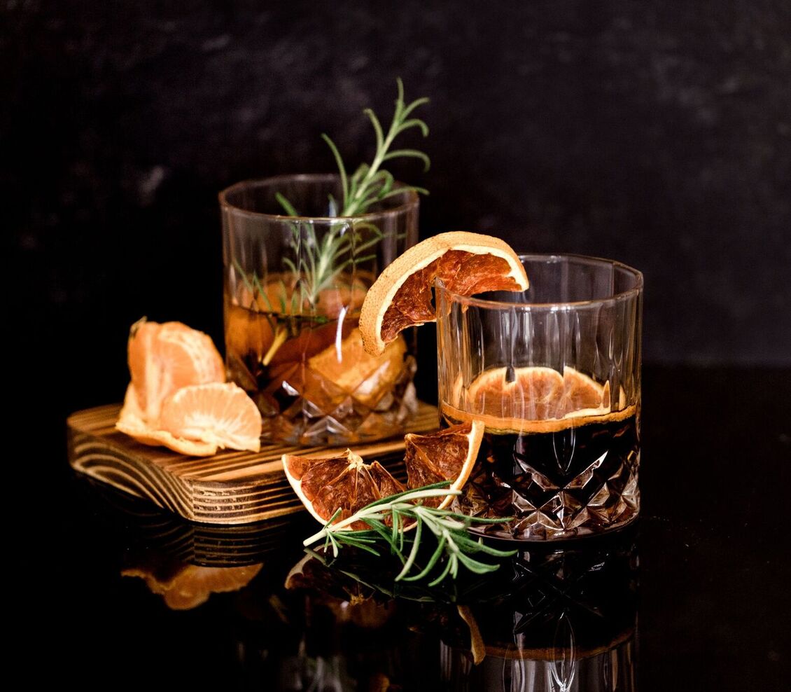 Dwa kryształowe koktajle z suszonymi plasterkami cytrusów i rozmarynem na drewnianej desce z mandarynkami, ciemne, nastrojowe tło