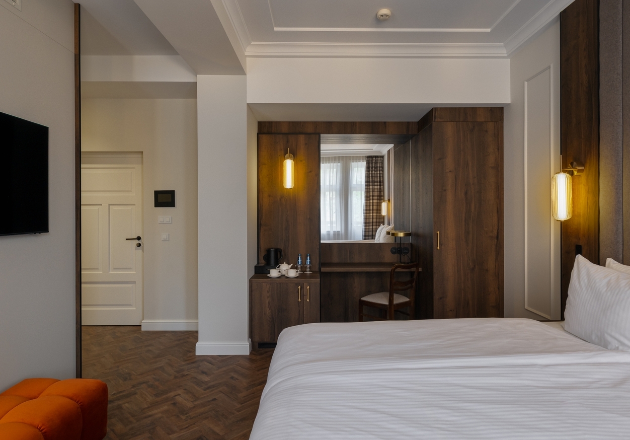 Nowoczesny pokój z łóżkiem king, tapicerowanym wezgłowiem, ciepłymi kinkietami, drewnianą szafą, biurkiem i telewizorem.