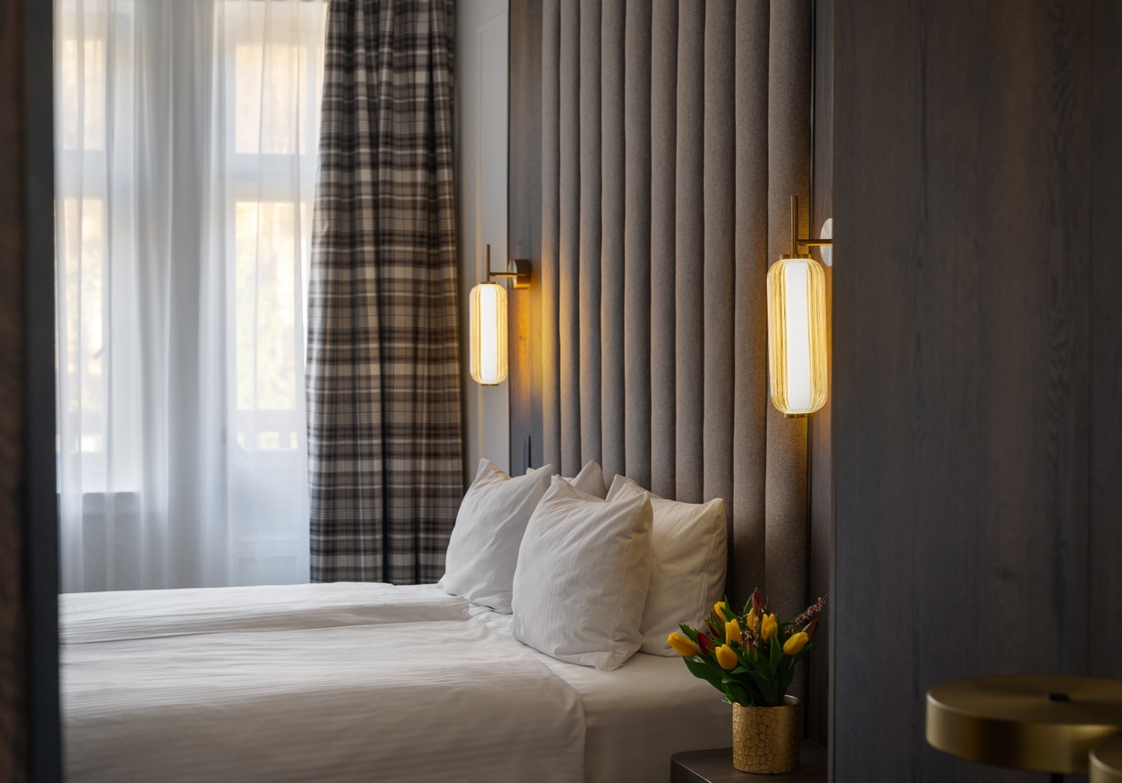 Nowoczesny pokój hotelowy z dwoma łóżkami pojedynczymi, wysokim tapicerowanym zagłówkiem, ciepłymi lampami, zasłonami w kratę i tulipanami na stoliku nocnym