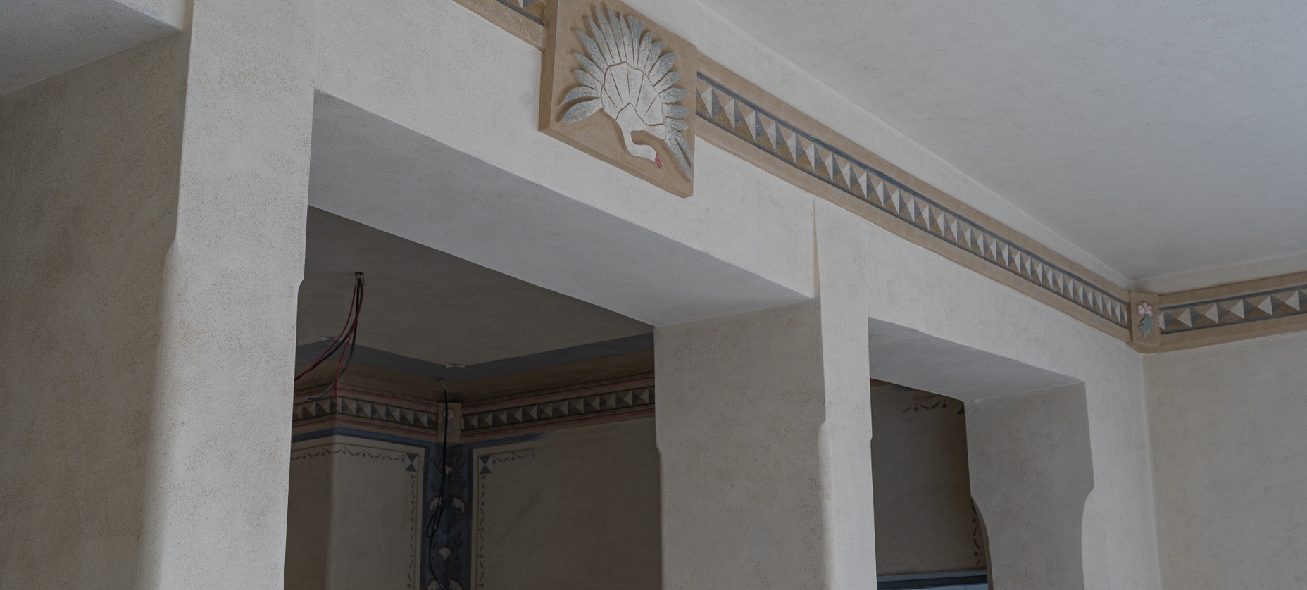 Tynkowane arkady z ozdobnym geometrycznym fryzem i rzeźbionym motywem wachlarza nad przejściem, stonowana kolorystyka