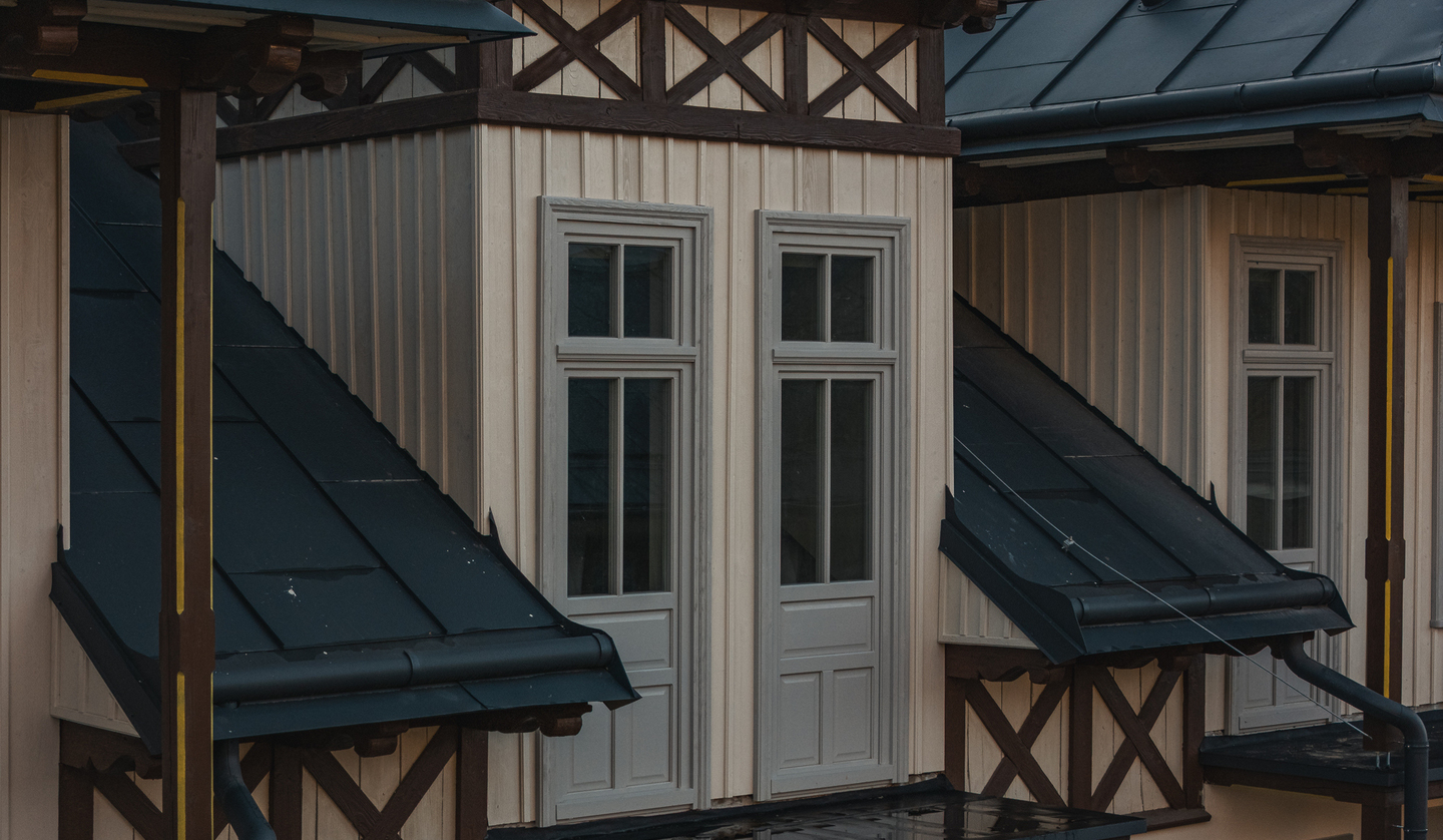 Elewacja hotelu w stylu alpejskim z kremową drewnianą okładziną, ciemnymi dachami przyokiennymi i wysokimi oknami