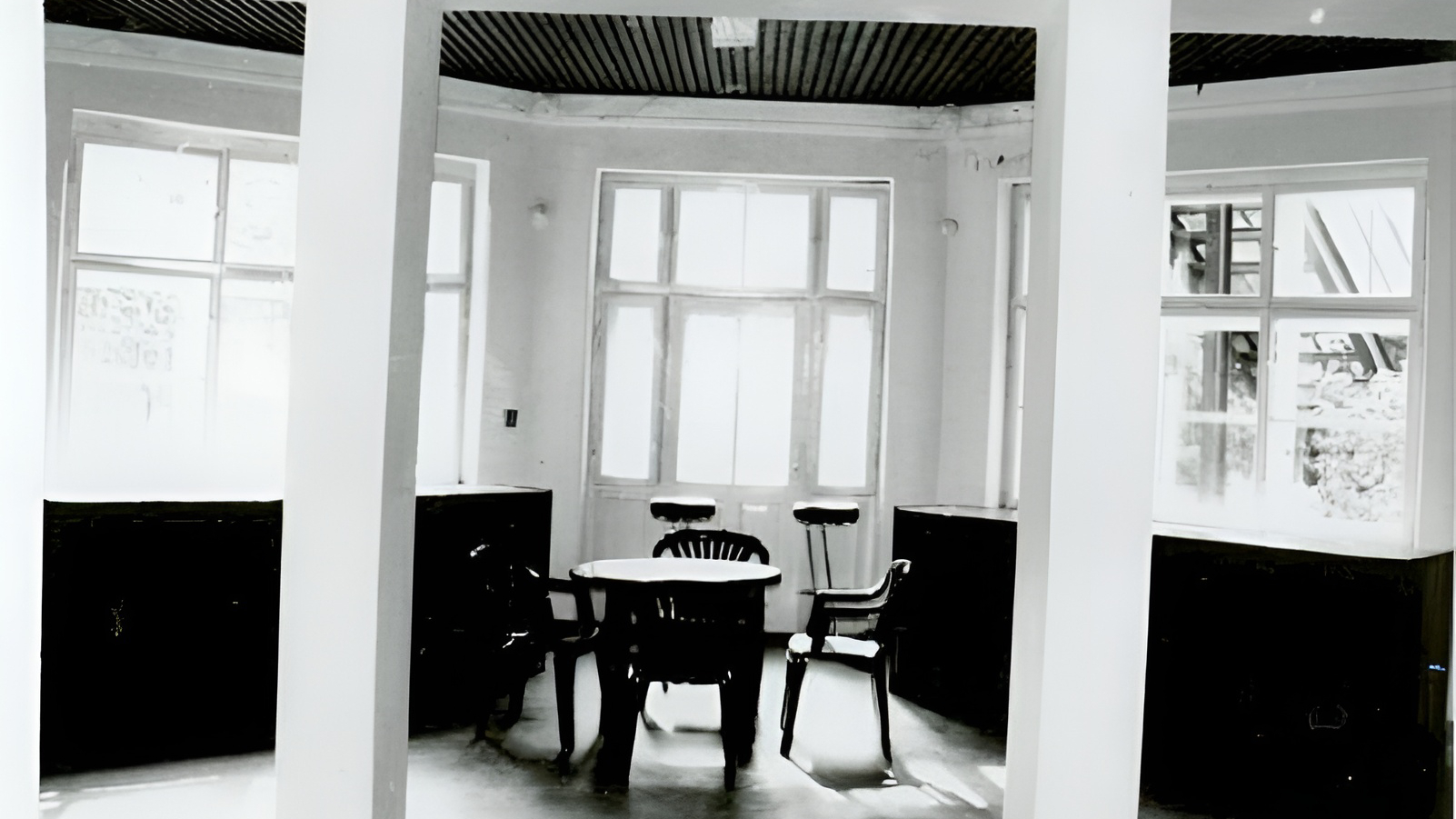 Słoneczny zakątek śniadaniowy hotelu z okrągłym stołem, krzesłami i stołkami barowymi przy wysokich oknach, drewniany sufit