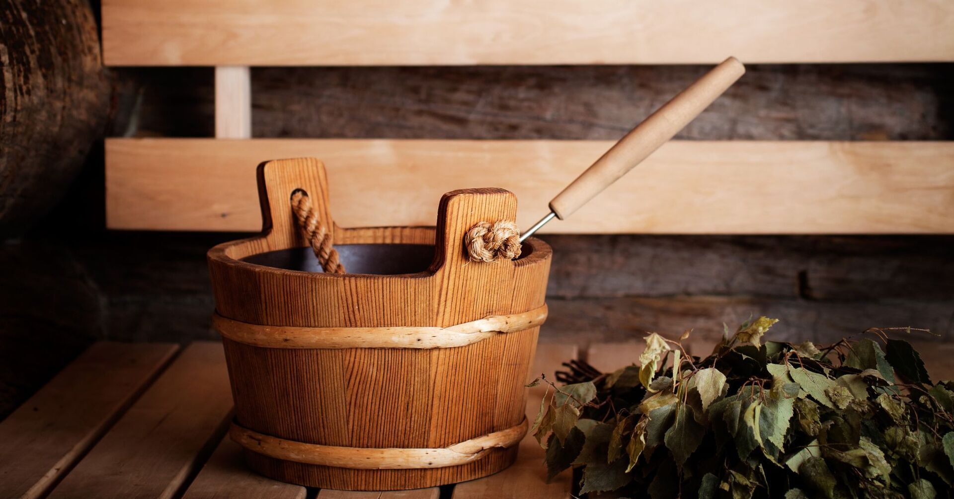 Drewniane wiadro do sauny z nabierakiem i wiązką brzozowych gałązek na ławce w rustykalnej saunie