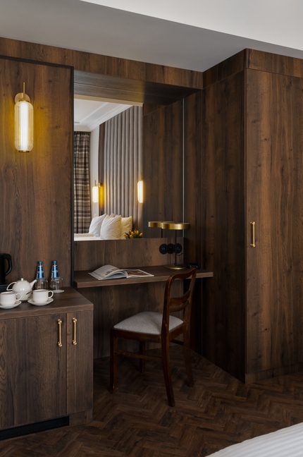 Przytulny pokój z drewnianymi panelami, biurkiem i krzesłem, mosiężnymi lampami, zestawem do herbaty i wodą, pikowanym zagłówkiem w lustrze.