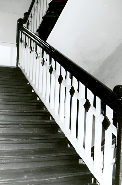 Drewniane schody wewnętrzne z ciemną poręczą i białymi słupkami z diamentowymi ozdobami, klasyczne wnętrze hotelowe.