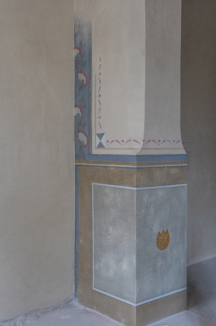 Dekoracyjna, malowana kolumna wewnętrzna z matowymi tynkami, niebiesko‑złotą opaską, kwiatowym motywem i małym złotym emblematem