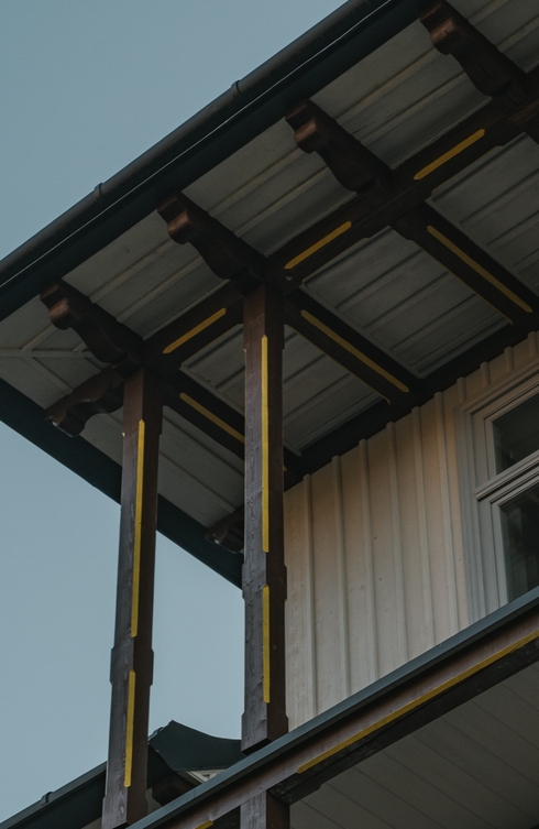 Fasada hotelu z drewnianymi słupami balkonu, ozdobnymi belkami i zadaszonym tarasem na piętrze