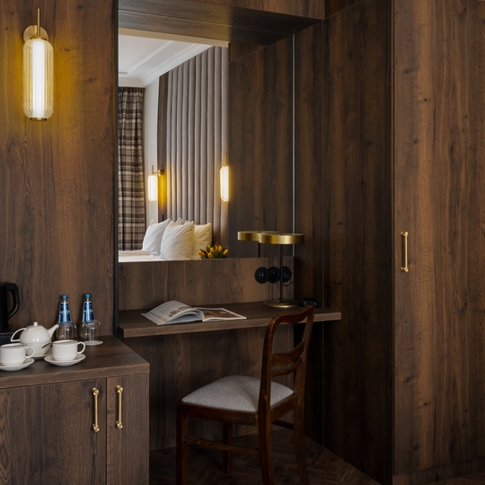 Przytulny pokój z drewnianymi panelami, biurkiem i krzesłem, mosiężnymi lampami, zestawem do herbaty i wodą, pikowanym zagłówkiem w lustrze.