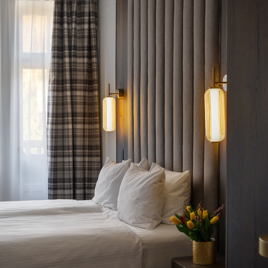 Nowoczesny pokój hotelowy z dwoma łóżkami pojedynczymi, wysokim tapicerowanym zagłówkiem, ciepłymi lampami, zasłonami w kratę i tulipanami na stoliku nocnym