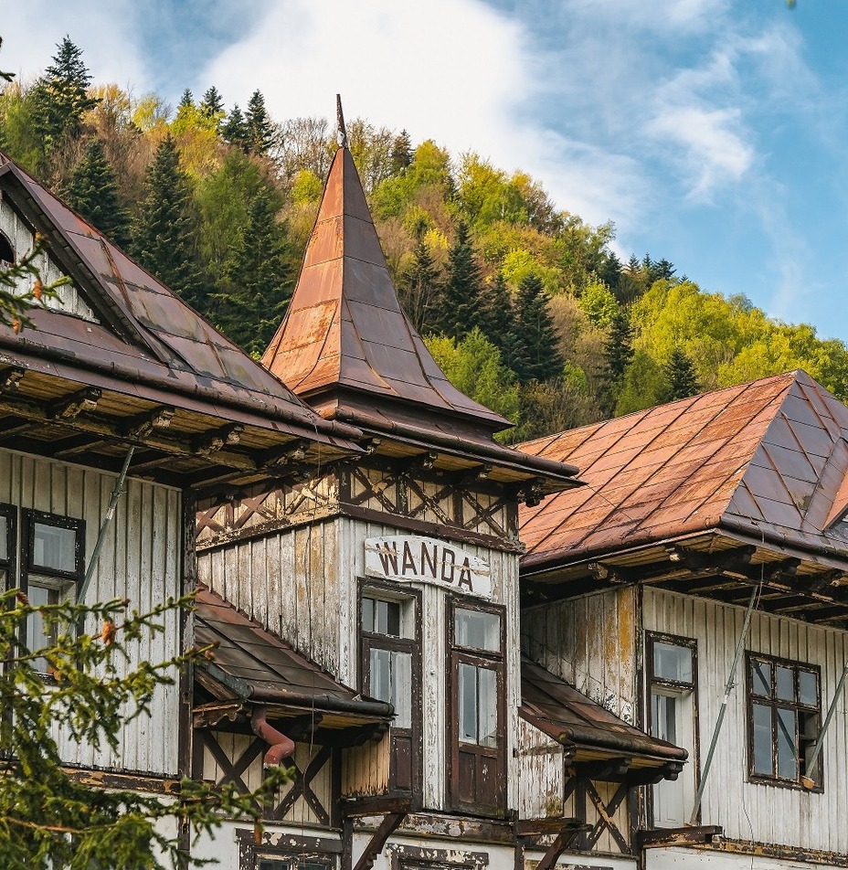 Zabytkowa górska willa 'Wanda' z miedzianymi, spadzistymi dachami, drewnianymi balkonami i widokiem na zalesione wzgórza.