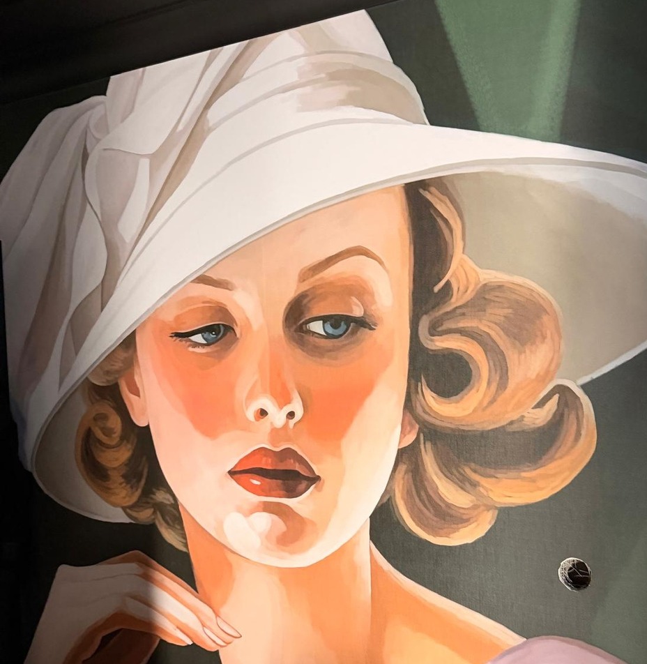 Duży mural portretujący elegancką kobietę w białym kapeluszu, retro fale włosów, delikatne brzoskwiniowe i zielone tony.