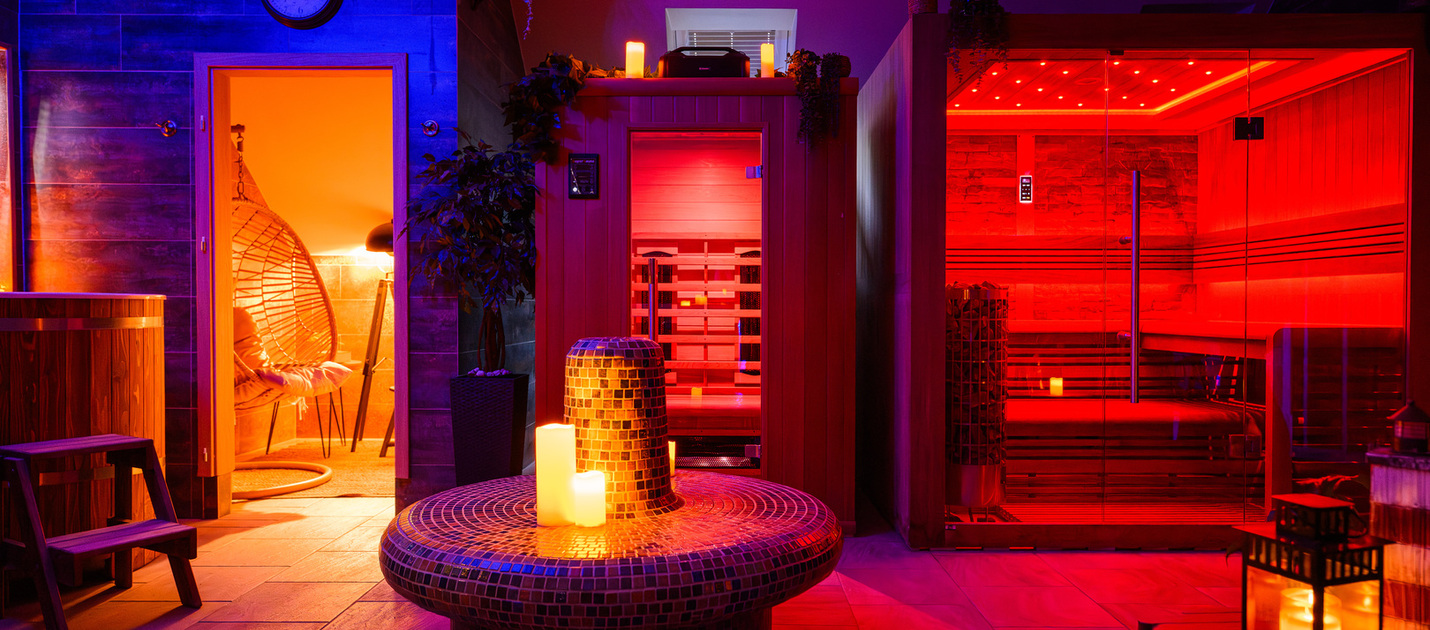 Rot beleuchtete Glas-Saunakabine, mosaikbeheizte Sitzbank mit Kerzen, hängender Rattansessel und hölzerne Wanne im stimmungsvollen Spa.