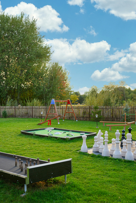 Outdoor hotel games lawn with giant chess set, mini-golf putting greens, swing and lawn bowling by trees and wooden fence
