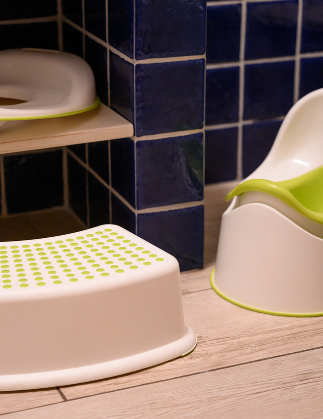 Child-friendly bathroom set with white-and-green potty, non-slip step stool and toddler toilet seat beside a blue-tiled wall