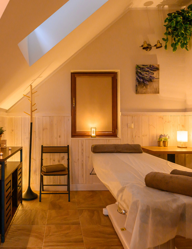 Przytulny pokój spa na poddaszu z łóżkiem do masażu, światłem świec, drewnianą boazerią i roślinami