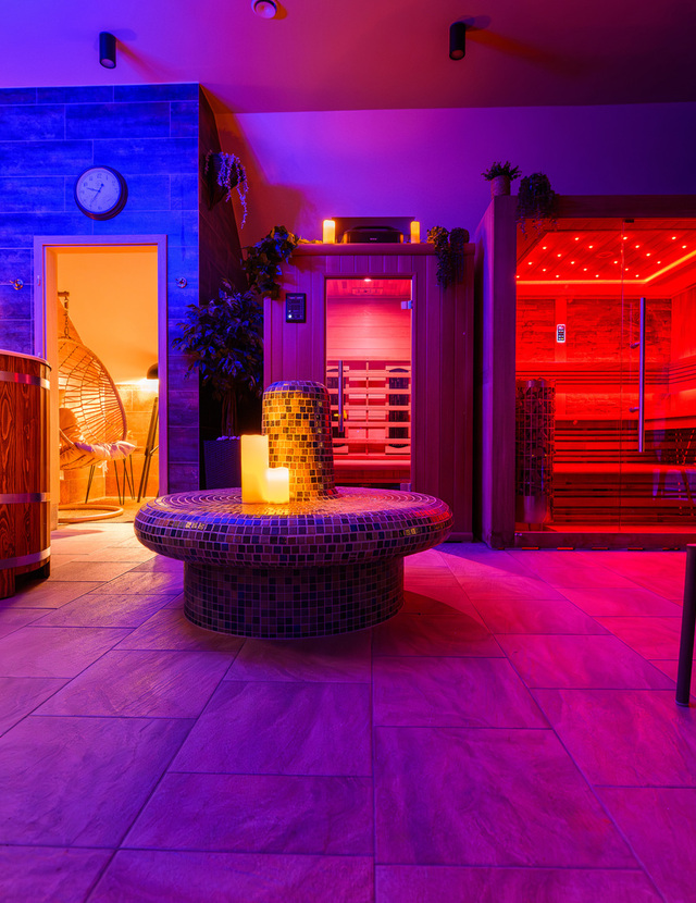 Privater Spa-Bereich mit rot beleuchteter Glas-Sauna, hölzernem Tauchbecken, Mosaik-Sitzinsel mit Kerzen und Hängesessel