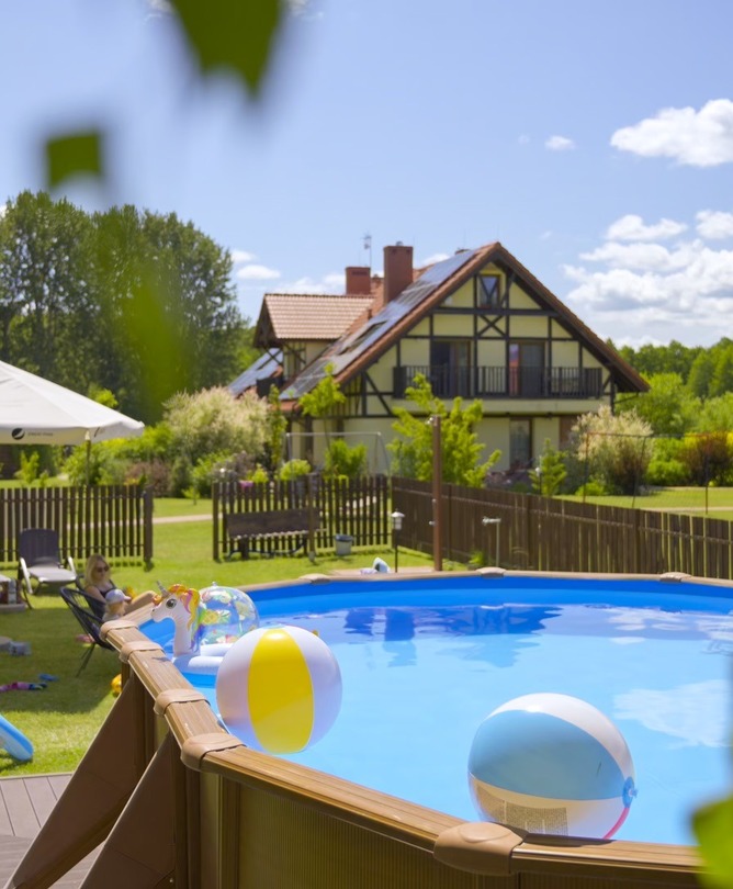 Above-ground pool with beach balls and inflatables, lawn sunloungers and umbrella, chalet-style guesthouse and garden