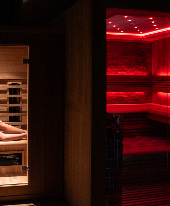 Drewniana prywatna sauna z ciepłym czerwonym oświetleniem LED, zwiniętymi ręcznikami i gościem odpoczywającym na ławce.