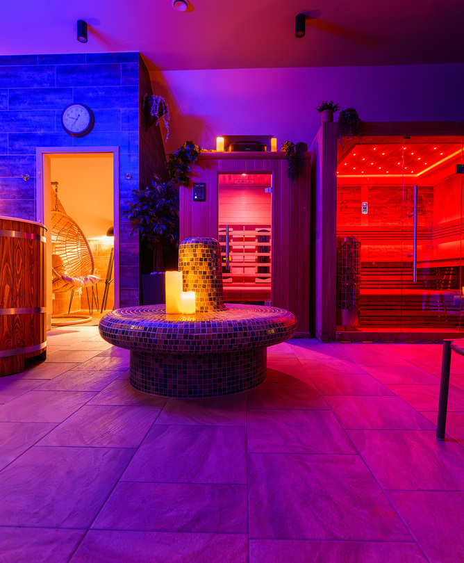 Privater Spa-Bereich mit rot beleuchteter Glas-Sauna, hölzernem Tauchbecken, Mosaik-Sitzinsel mit Kerzen und Hängesessel