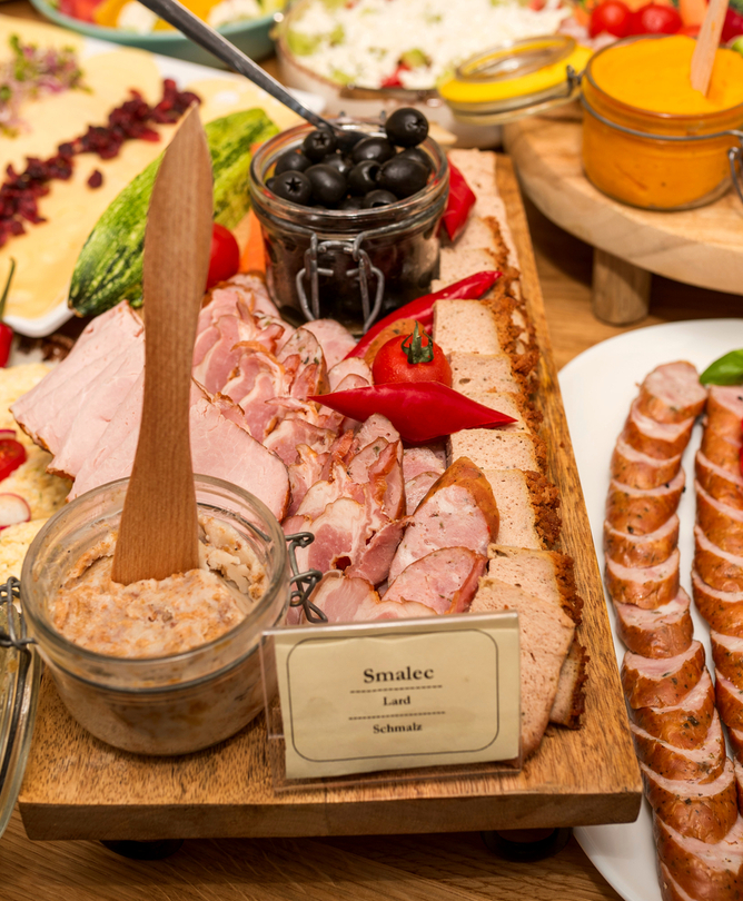Rustiškas bufetas su pjaustyta mėsa ir dešromis, paštetu ir stiklainiu smalco, juodomis alyvuogėmis, kiaušinių pasta ir pomidorais su baziliku.