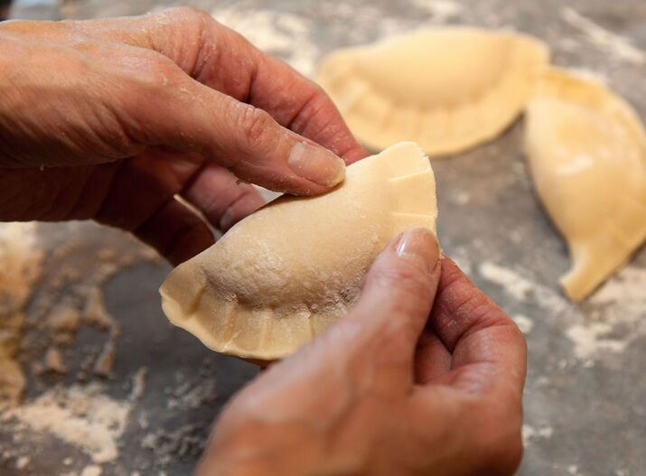 Ręce formują pierogi na obsypanym mąką blacie — przygotowanie domowych pierogów.
