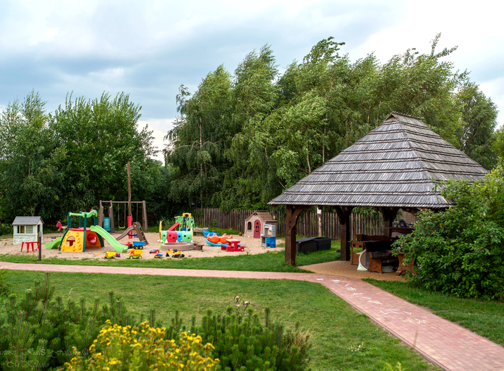 Familienfreundlicher Außen-Spielplatz mit bunten Rutschen, Schaukeln und Sandkasten neben Holzpavillon und Rasen.