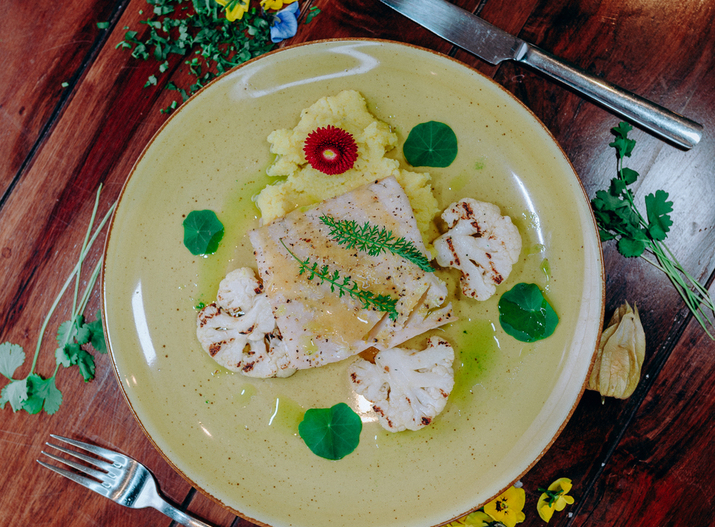 Smażony filet z białej ryby na kremowym puree, grillowany kalafior, ziołowy olej i jadalne kwiaty na rustykalnym stole