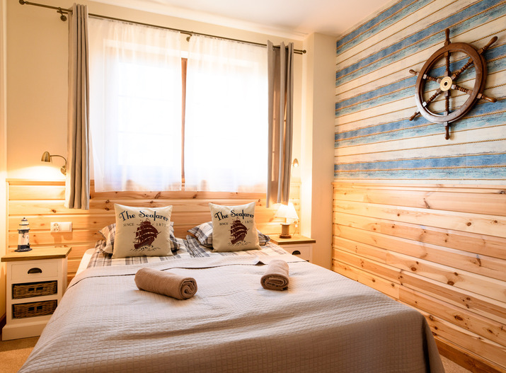 Gemütliches Doppelzimmer im maritimen Stil mit Holzverkleidung, Schiffsteuerrad, Nachttischlampen, 'The Seafarer'-Kissen und aufgerollten Handtüchern