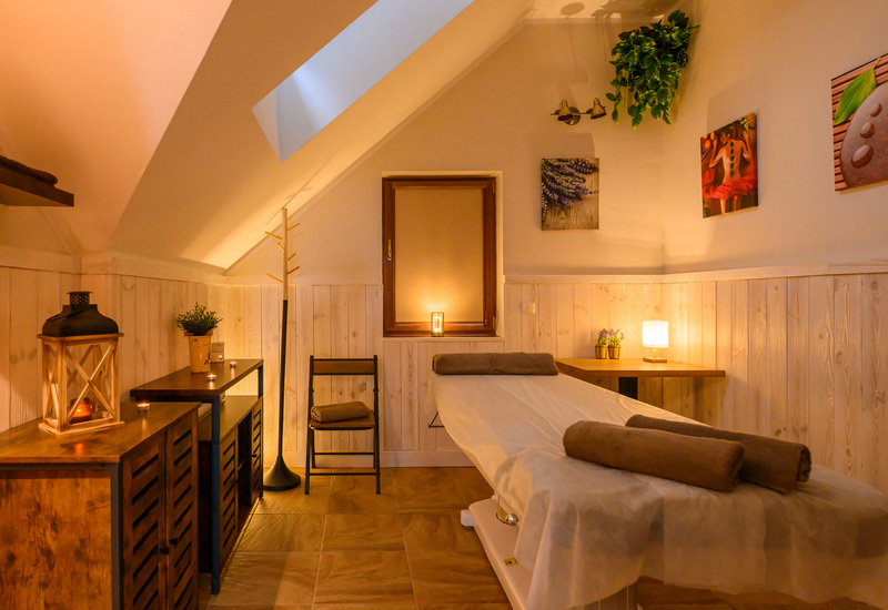 Jauki SPA palėpės patalpa su masažo stalu, žvakėmis, medine apdaila ir kambariniais augalais