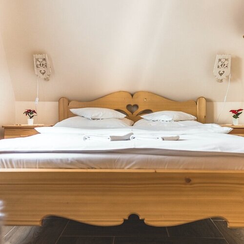 Cozy attic double room with pine bed (heart-cut headboard), white linens, bedside tables, reading lamps and green curtain
