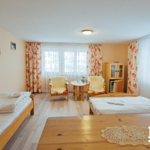 Bright twin room with wooden beds, floral curtains, two sheepskin-covered armchairs, round table and cabinet with mini-fridge