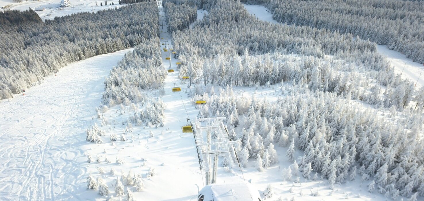 Widok z gondoli na ośnieżone stoki narciarskie i las iglasty w zimowej scenerii kurortu narciarskiego