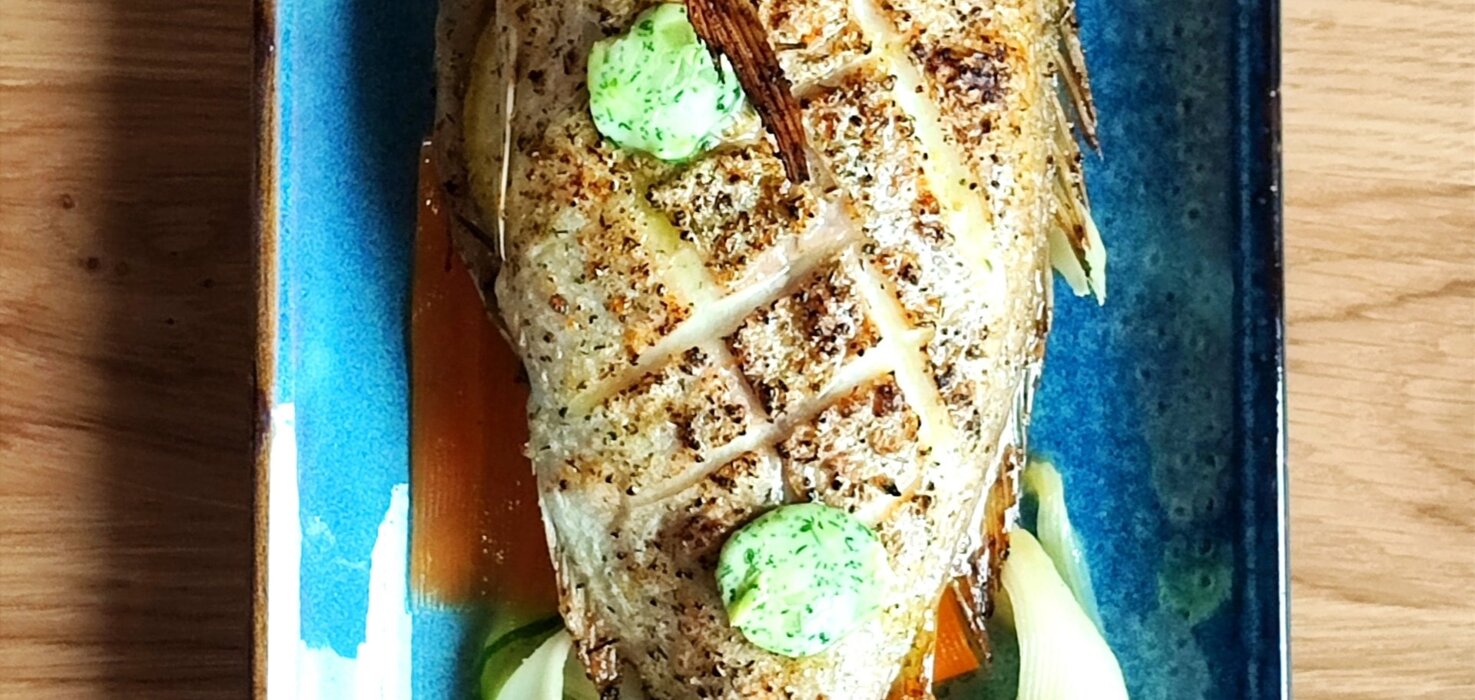 Grillowana ryba podana na niebieskim talerzu z plastrami cytryny i warzywami, doprawiona ziołowym masłem