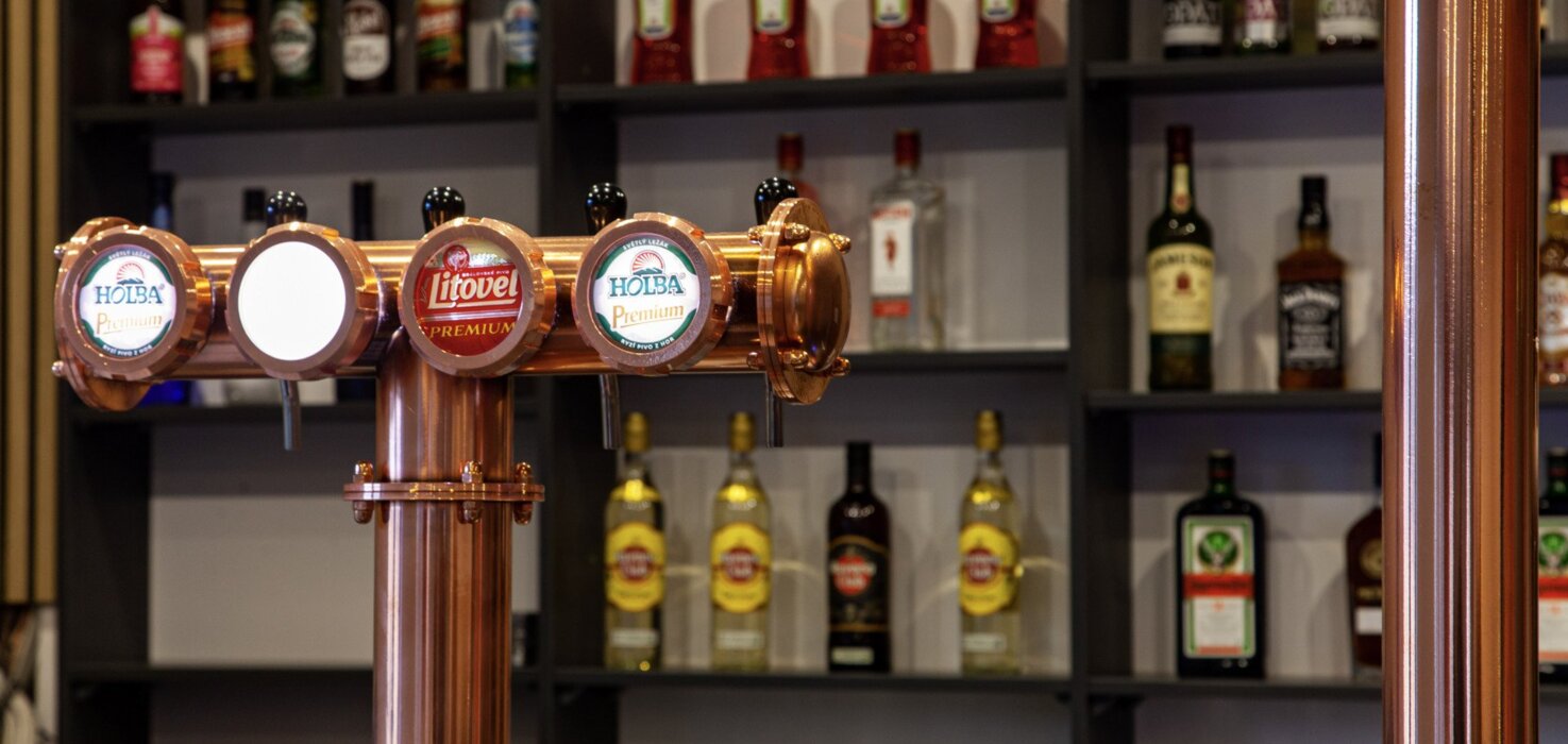 Miedziana kolumna z czterema kranami do piwa w barze z półkami pełnymi różnych butelek alkoholu w tle