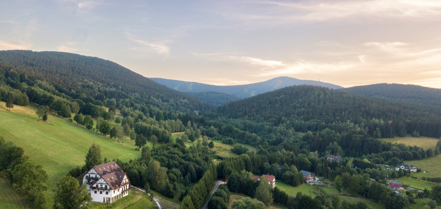 Dom wypoczynkowy w zielonej dolinie z widokiem na zalesione góry i spokojny wiejski krajobraz o zachodzie słońca