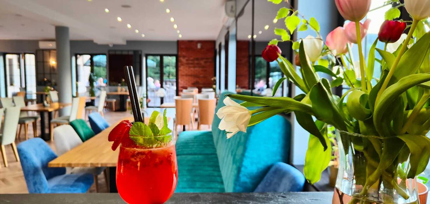 Nowoczesna sala restauracyjna z wygodnymi kolorowymi krzesłami, koktajlem z miętą i truskawkami oraz bukietem tulipanów na blacie