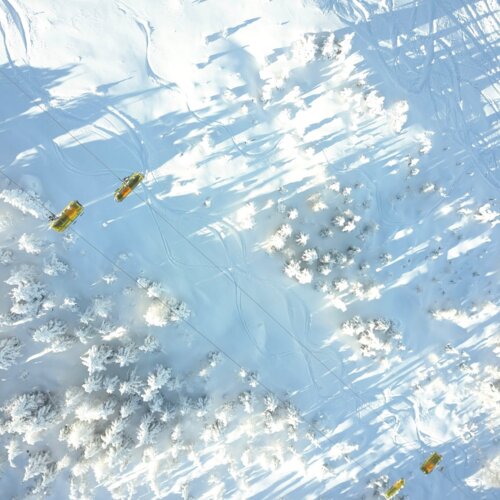 Widok z góry na ośnieżone stoki narciarskie z żółtymi wyciągami krzesełkowymi i śniegiem pokrywającym drzewa