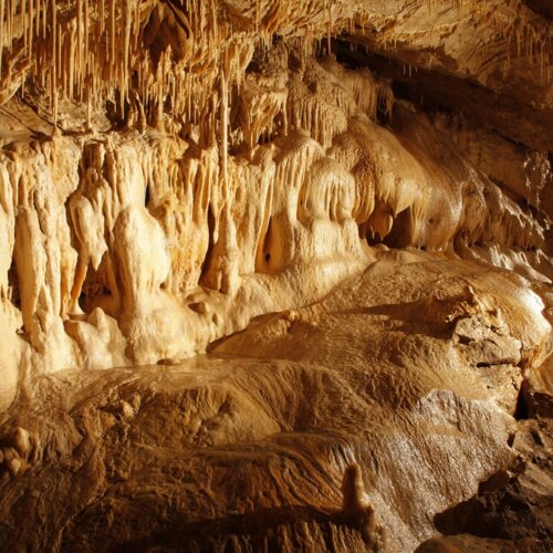 Widok na oświetloną jaskinię z pięknymi wapiennymi stalaktytami i stalagmitami tworzącymi naturalne formacje skalne